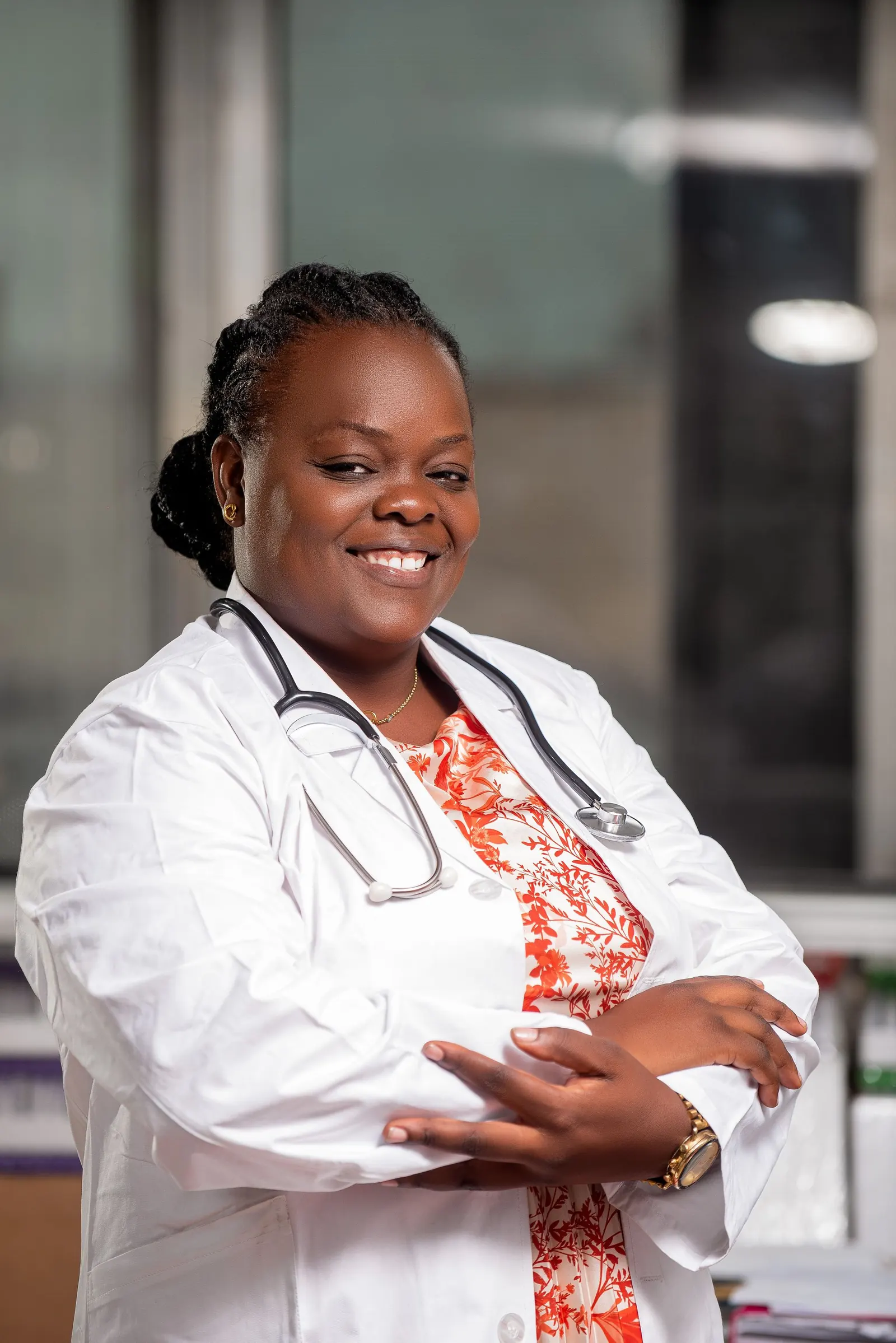 Smiling African female doctor in a white coat with a stethoscope, arms folded, in a clinic